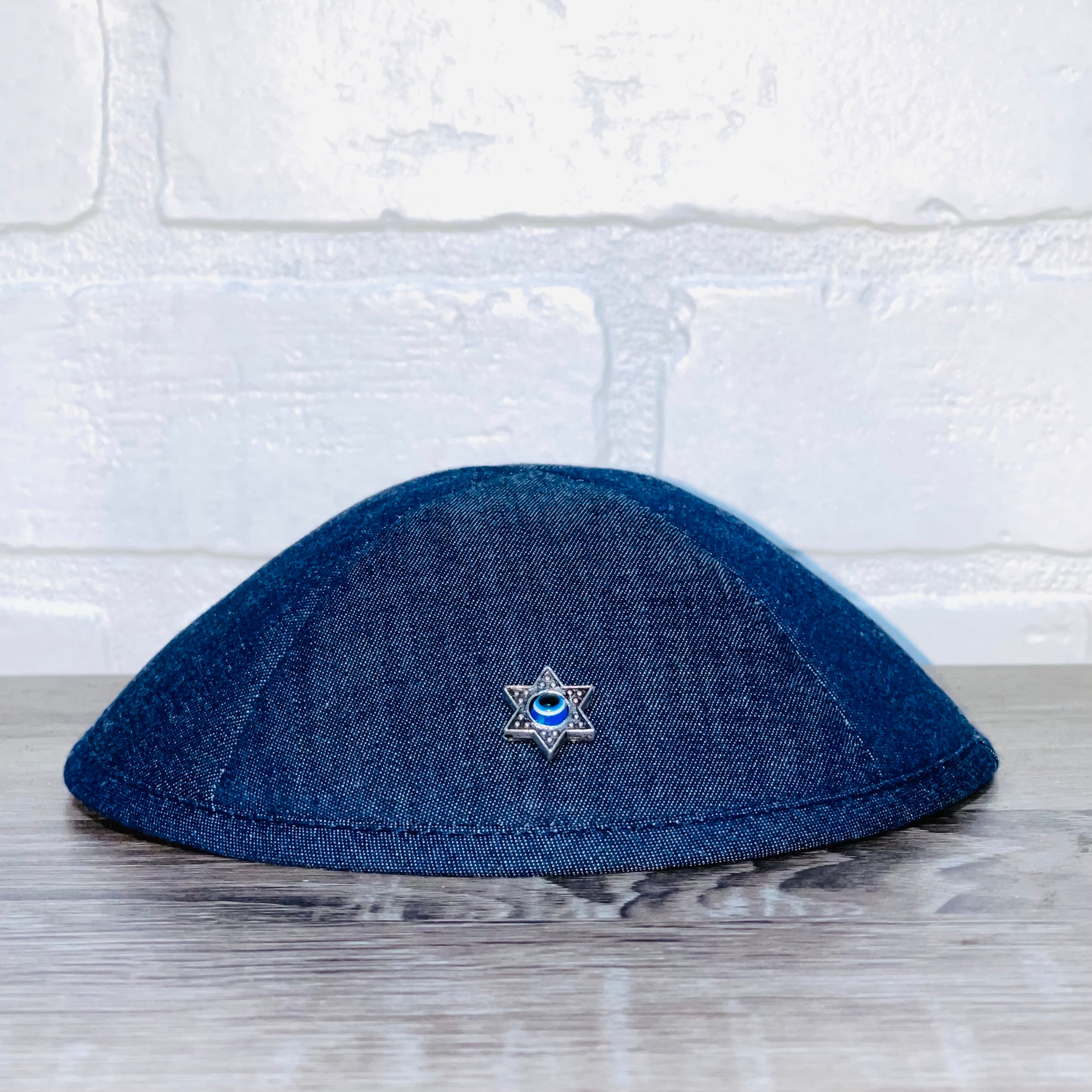 A beautifully crafted Magen David Kippah featuring a blue Evil Eye, available in black cotton, denim, and white linen.