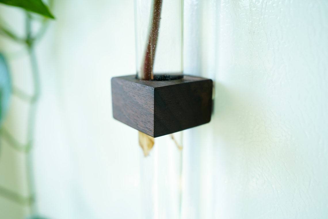 A stylish Magnetic Flower & Propagation Vase made from sustainably sourced Black Walnut, floating on a metal surface with flowers inside.