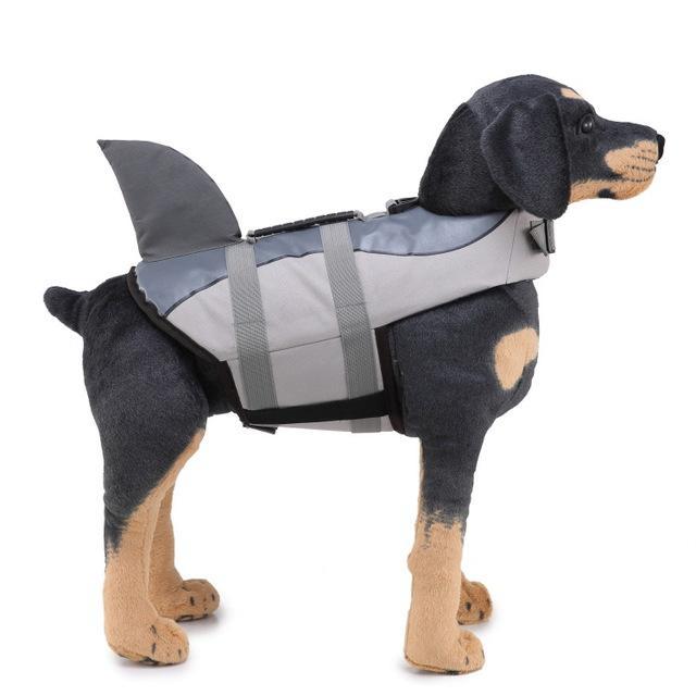 A small dog wearing a vibrant rose red and gray shark fin life jacket, floating in water, showcasing its buoyancy and stylish design.