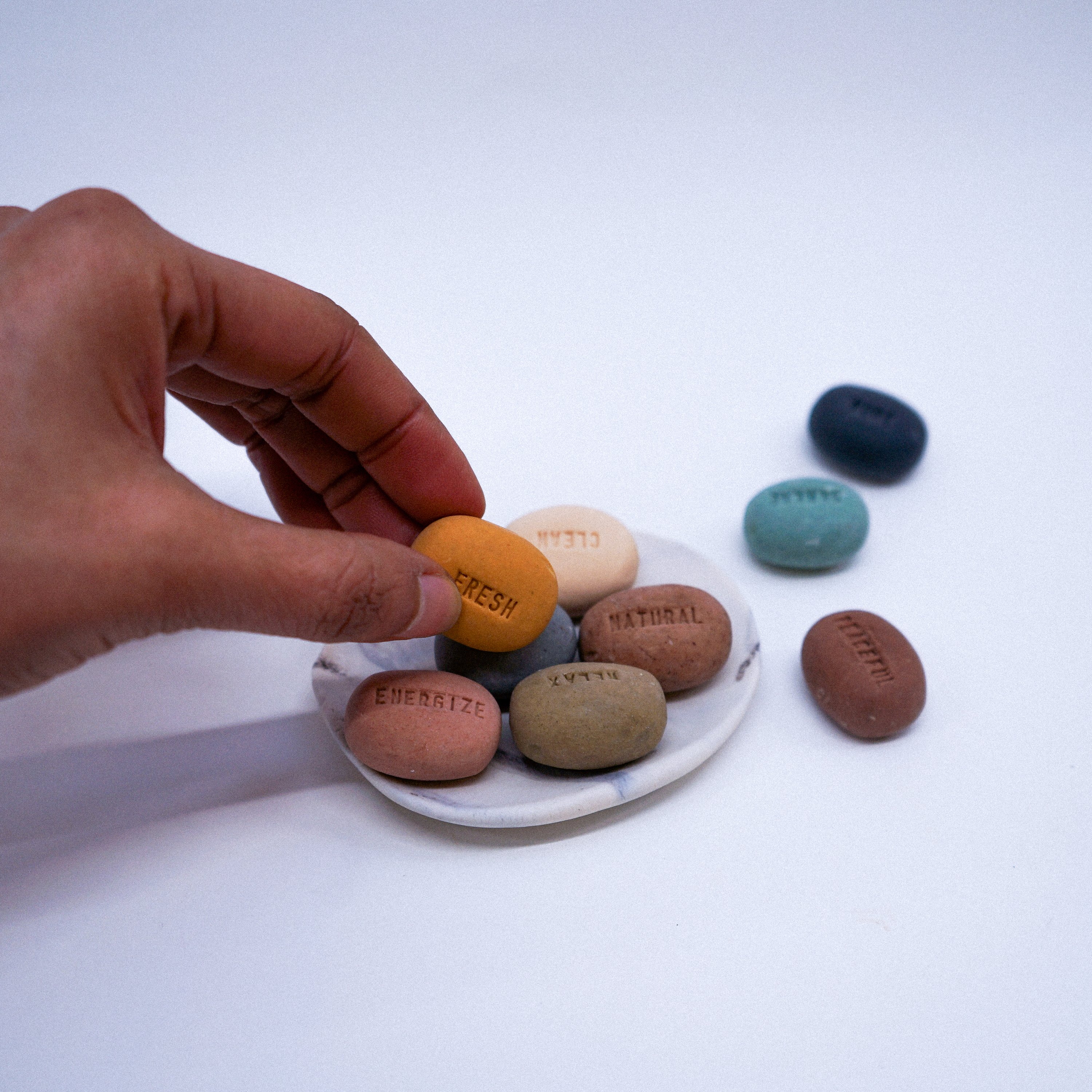 A collection of handmade Mood Soaps in pebble design with a white porcelain dish featuring a dark grey marble effect.