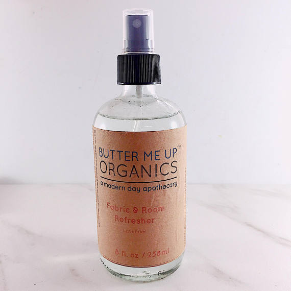 A bottle of Organic Fabric/Room Deodorizer Spray with a fresh and bright label, surrounded by natural elements like essential oils and plants.