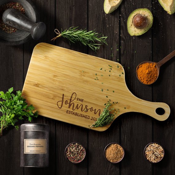 A personalized bamboo chopping board with a laser-etched design, showcasing its dual-purpose sides for food preparation and display, featuring a handle for easy hanging.