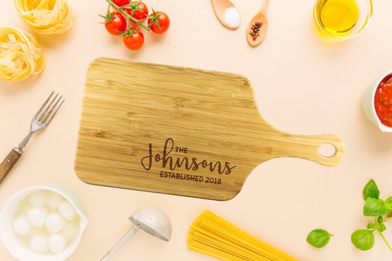 A personalized bamboo chopping board with a laser-etched design, showcasing its dual-purpose sides for food preparation and display, featuring a handle for easy hanging.