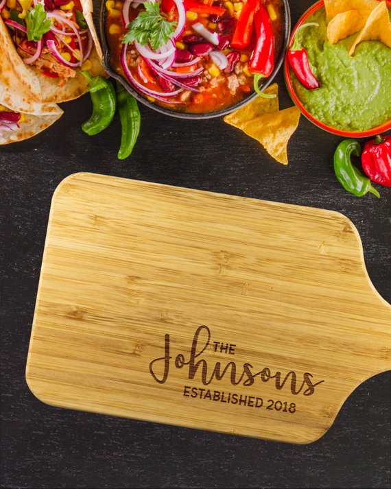 A personalized bamboo chopping board with a laser-etched design, showcasing its dual-purpose sides for food preparation and display, featuring a handle for easy hanging.