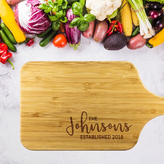 A personalized bamboo chopping board with a laser-etched design, showcasing its dual-purpose sides for food preparation and display, featuring a handle for easy hanging.