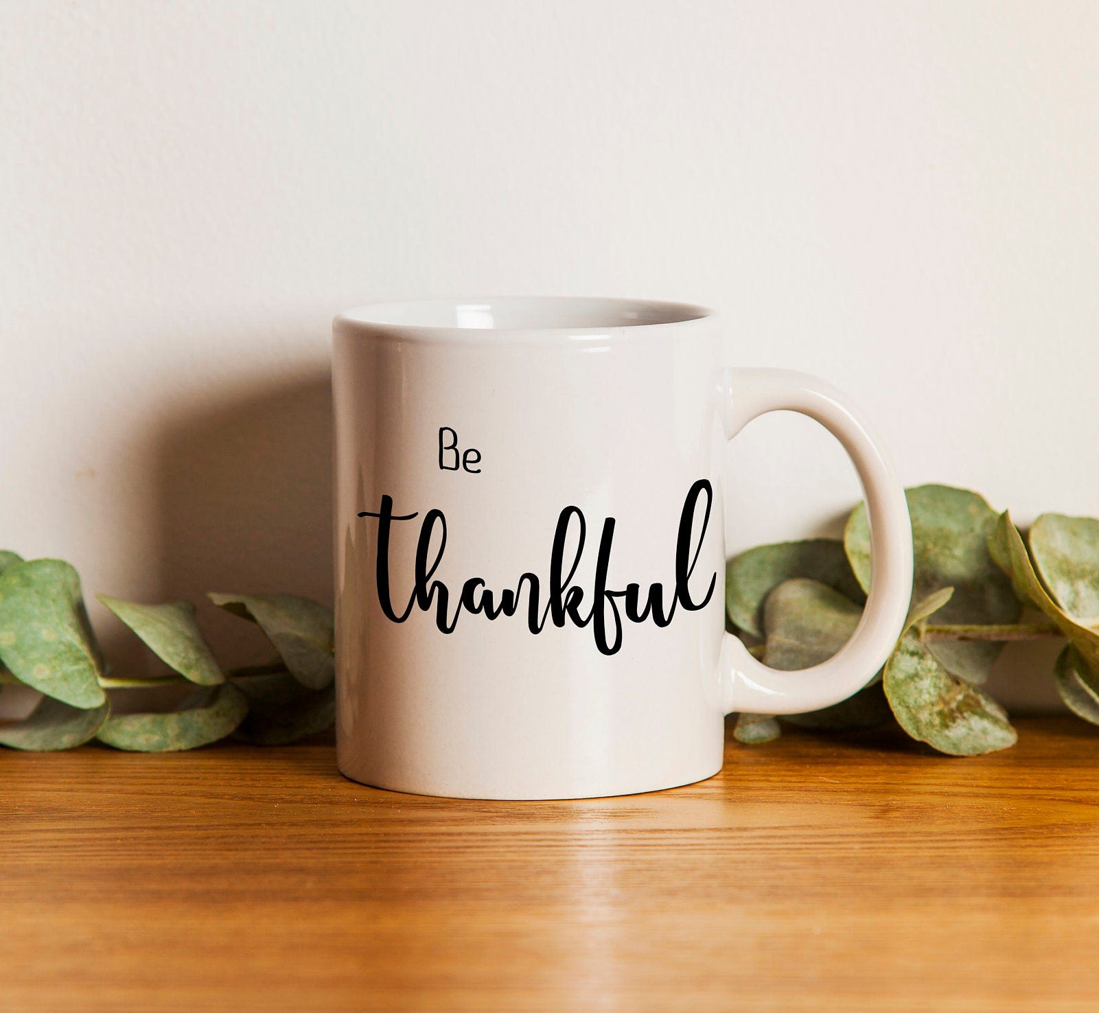 Personalized 'Be Thankful' coffee mug with hand-lettered design, available in two sizes, showcasing inspirational message.