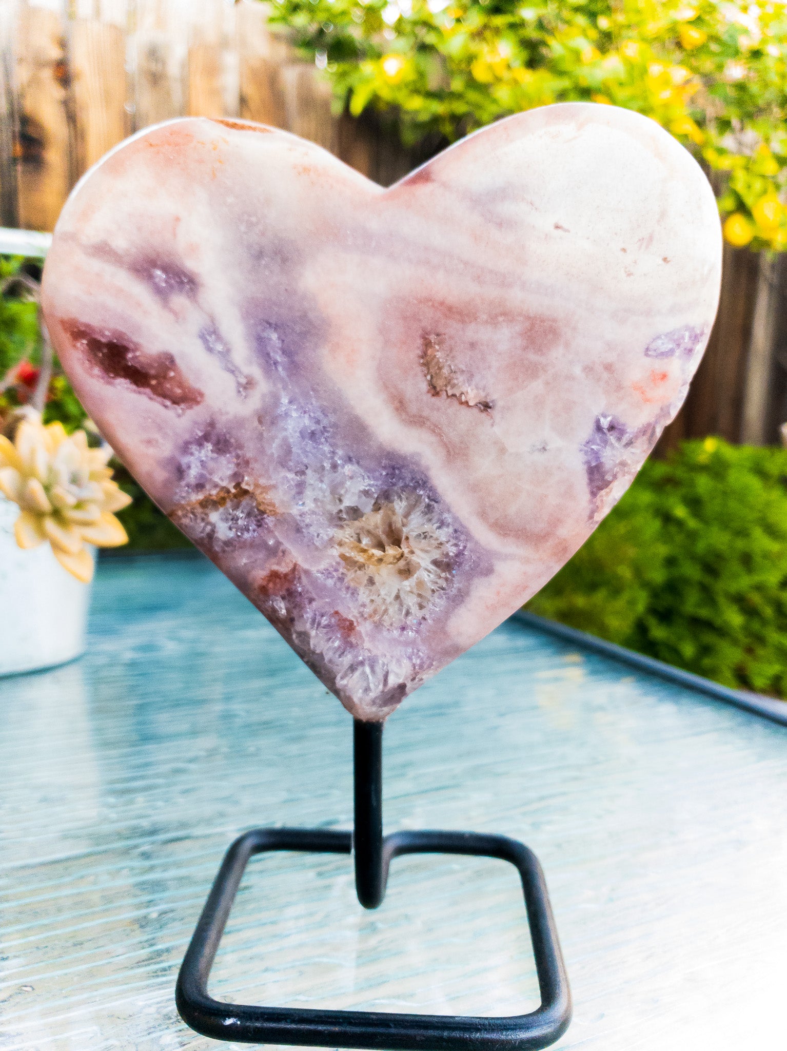 A polished Pink Amethyst heart displayed on a sleek metal stand, showcasing its beautiful pink hues and unique shape.