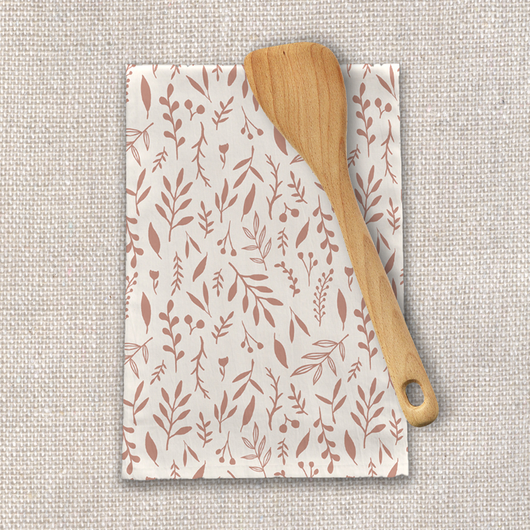 A pink tea towel featuring falling leaves design, made of cotton twill, perfect for kitchen use.