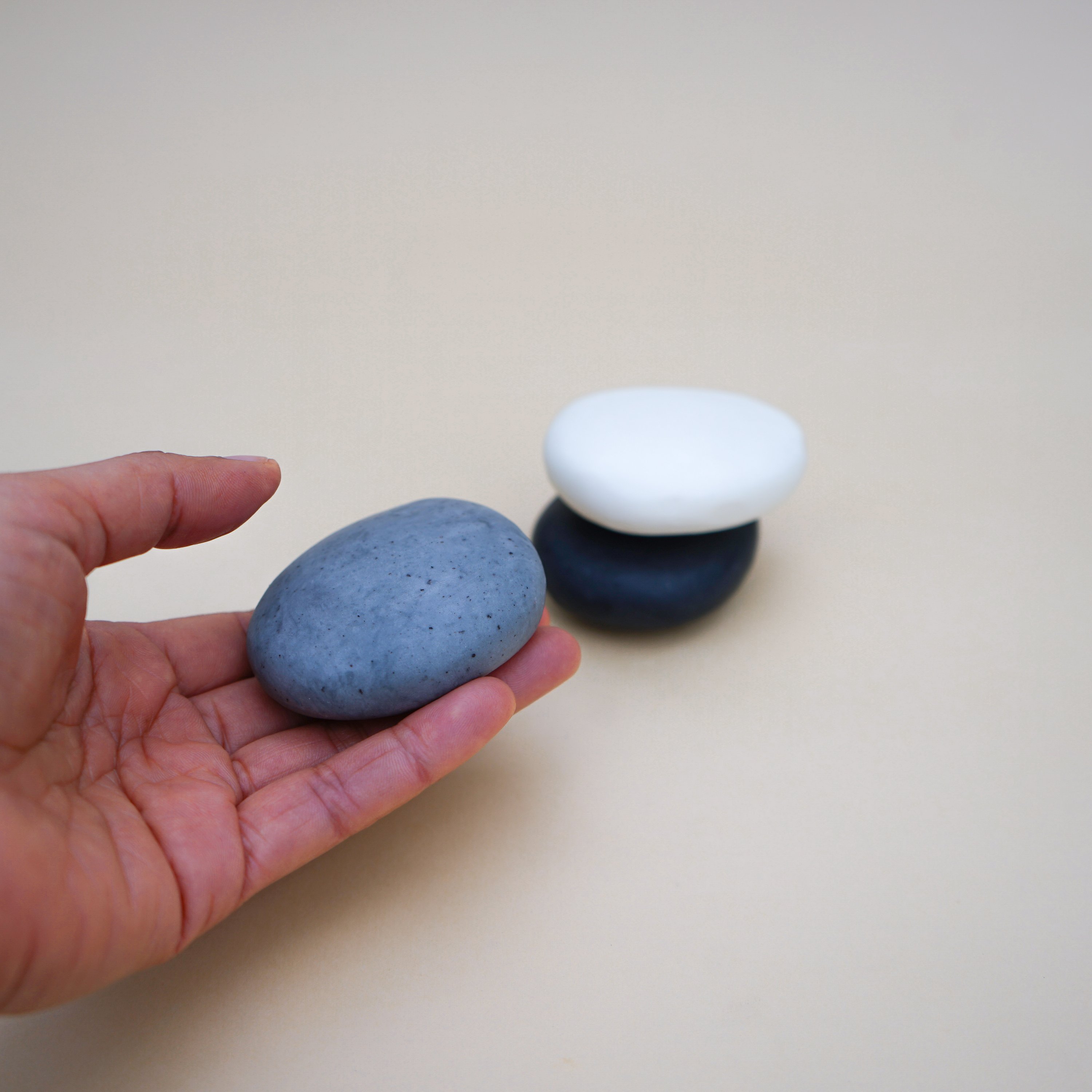 A collection of handmade Plain Colour Pebble Soaps in various natural colors, shaped like pebbles, displayed elegantly on a bathroom counter.