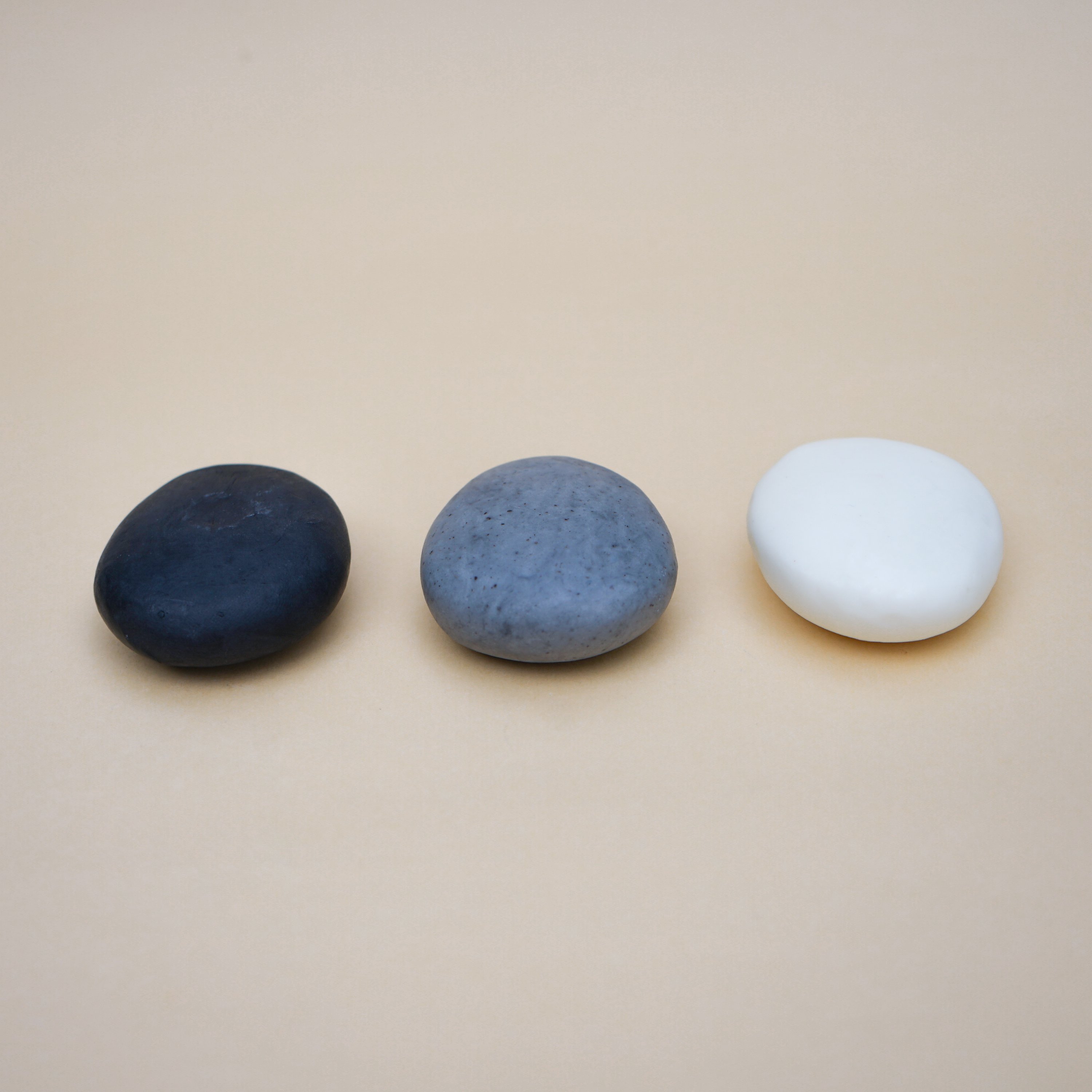 A collection of handmade Plain Colour Pebble Soaps in various natural colors, shaped like pebbles, displayed elegantly on a bathroom counter.