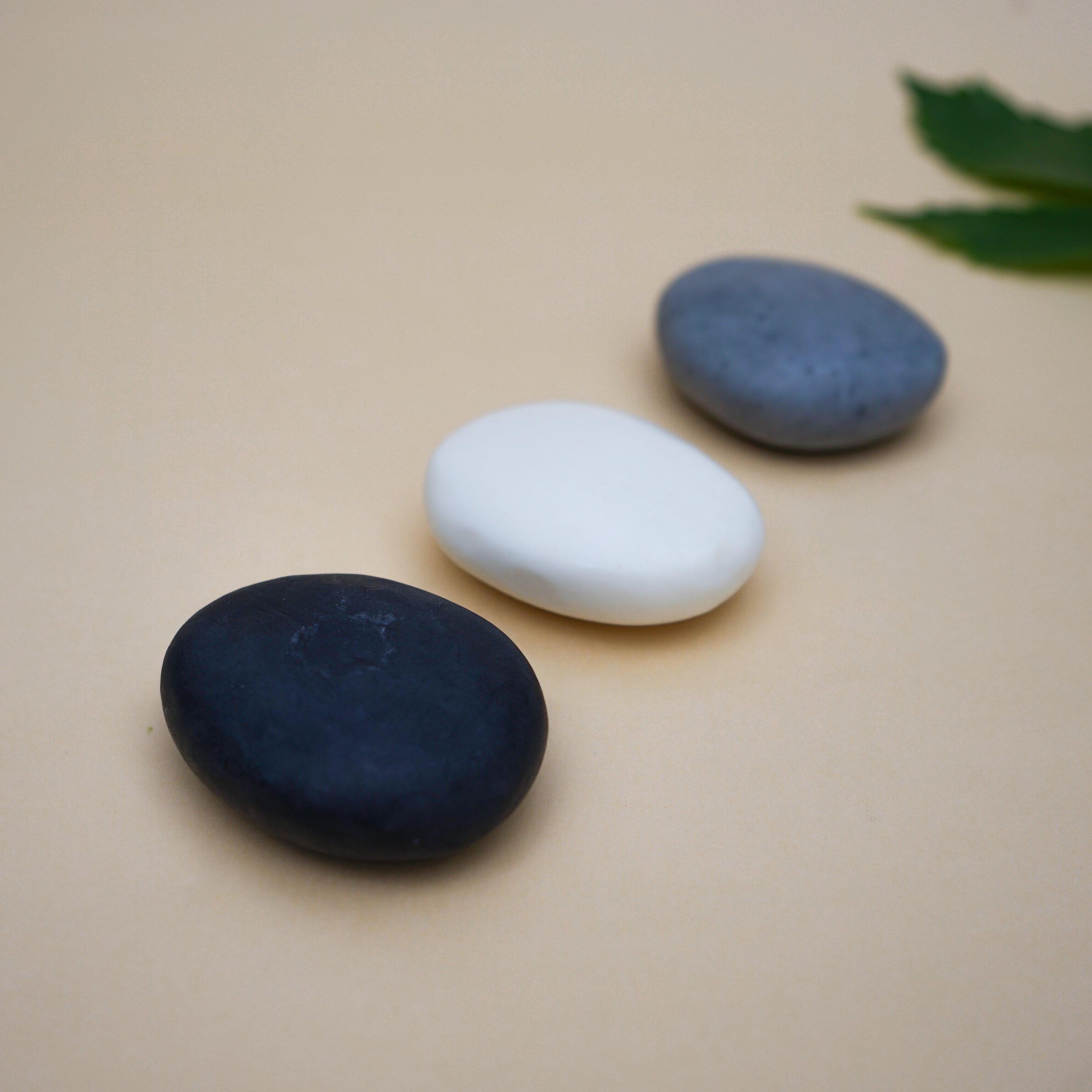 A collection of handmade Plain Colour Pebble Soaps in various natural colors, shaped like pebbles, displayed elegantly on a bathroom counter.