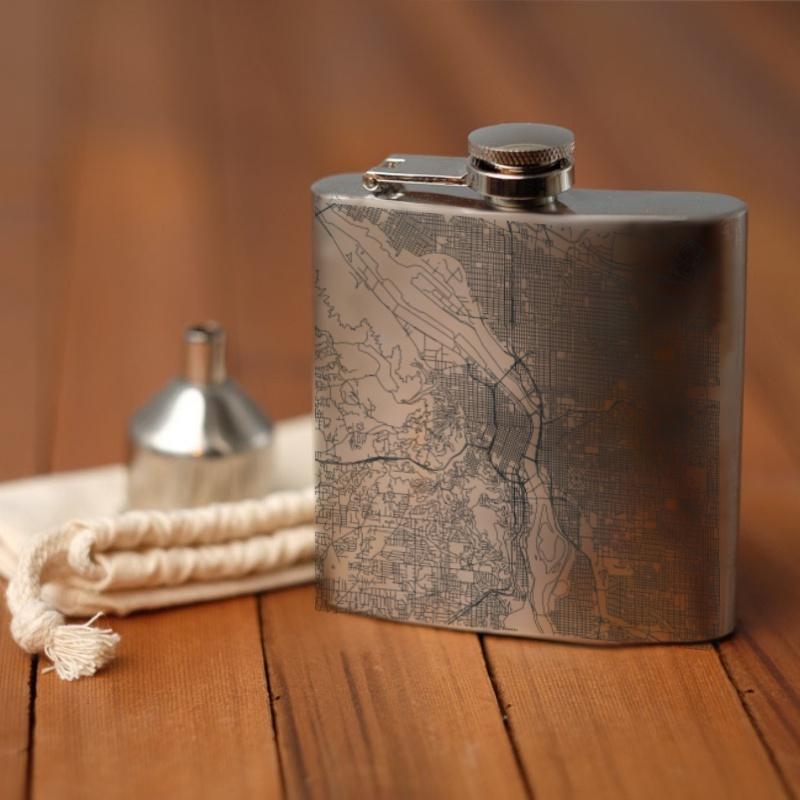 Custom engraved 6oz hip flask featuring a detailed map of Portland, Oregon with coordinates, accompanied by a canvas bag and funnel.