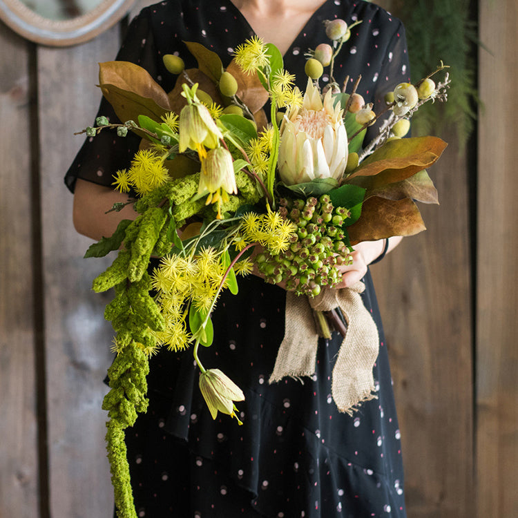 A 25-inch tall artificial bouquet featuring vibrant protea flowers, lush silk leaves, and eucalyptus seeds, arranged in a decorative style.