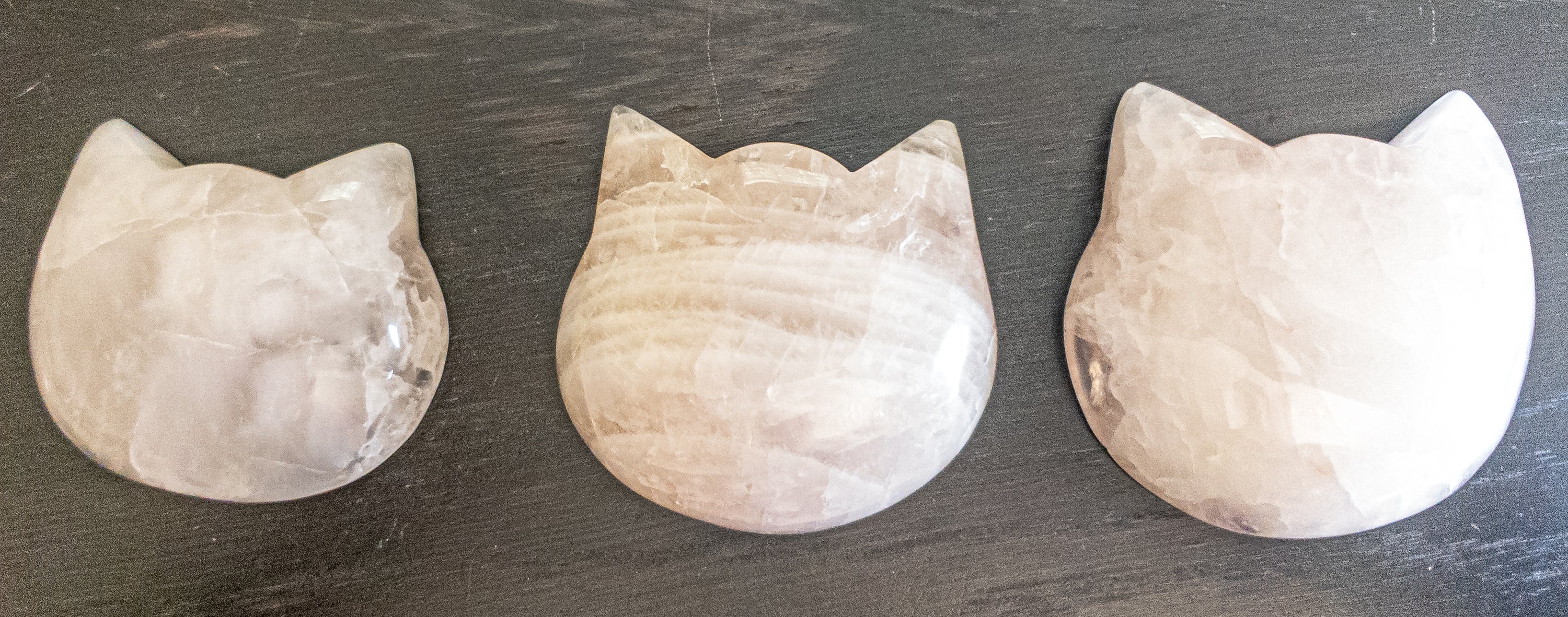 Three hand-polished Puffy Crystal Cat Heads in Black Obsidian, Rose Quartz, and Clear Quartz, showcasing their unique shapes and colors.