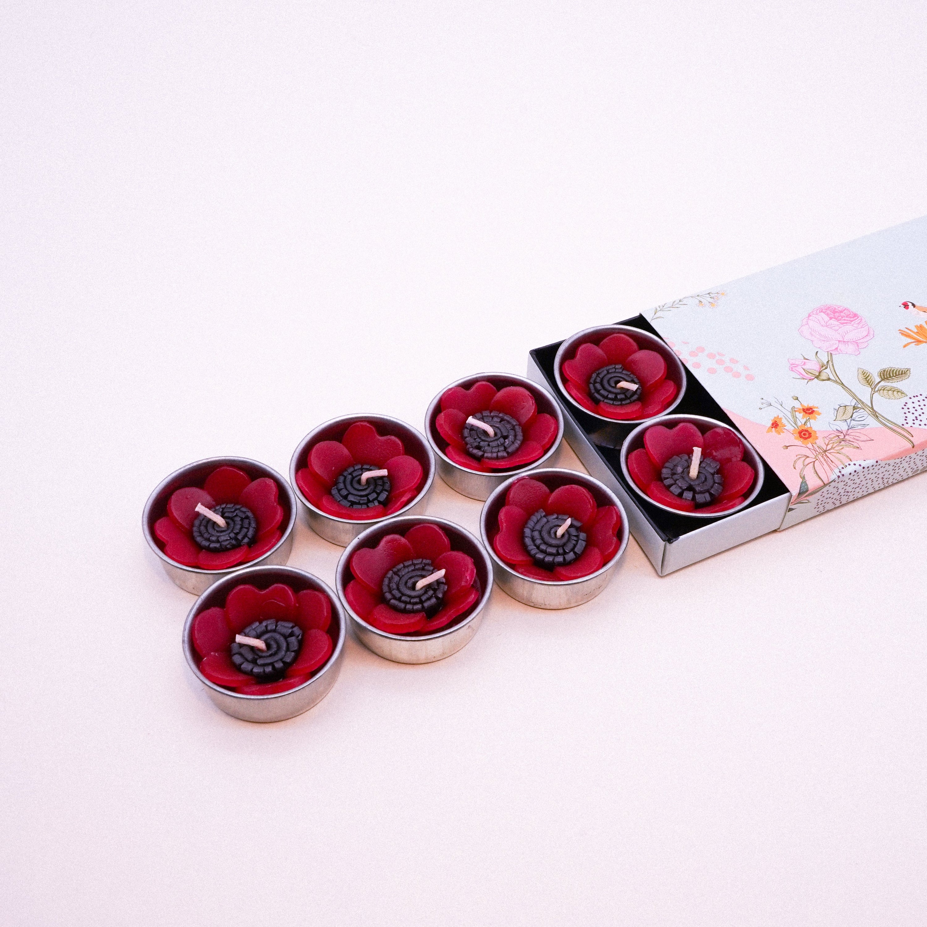 A set of eight red poppy scented tealights in a decorative botanical garden box, showcasing their vibrant color and unique flower shape.