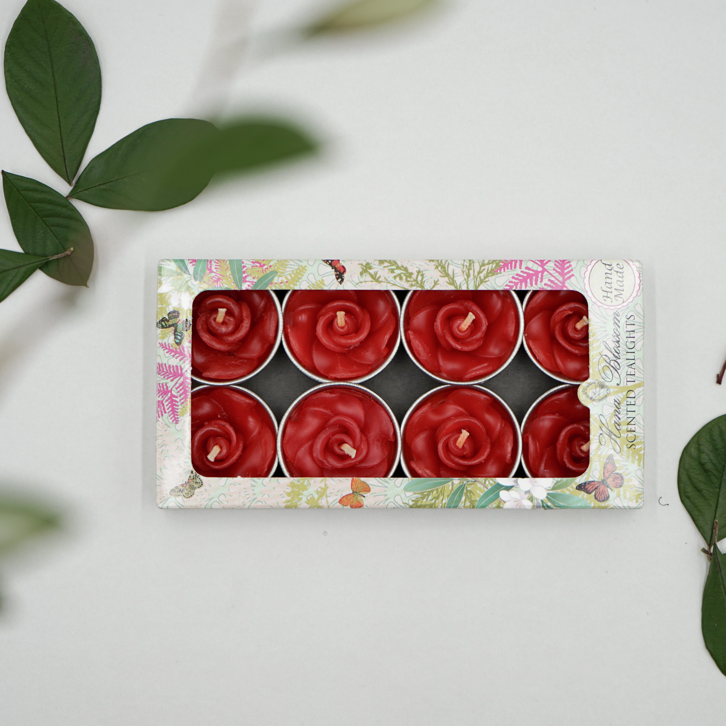 A set of eight red rose scented tealights in a decorative botanic garden printed box, showcasing their elegant design and vibrant color.