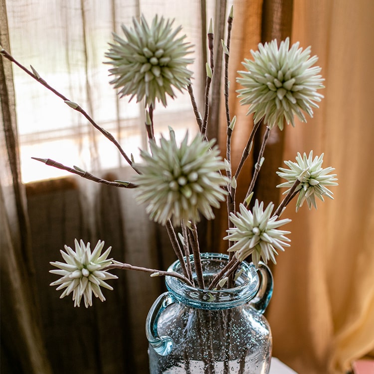 A vibrant green round ball flower on a twig stem, showcasing its handmade design and natural brown branches.