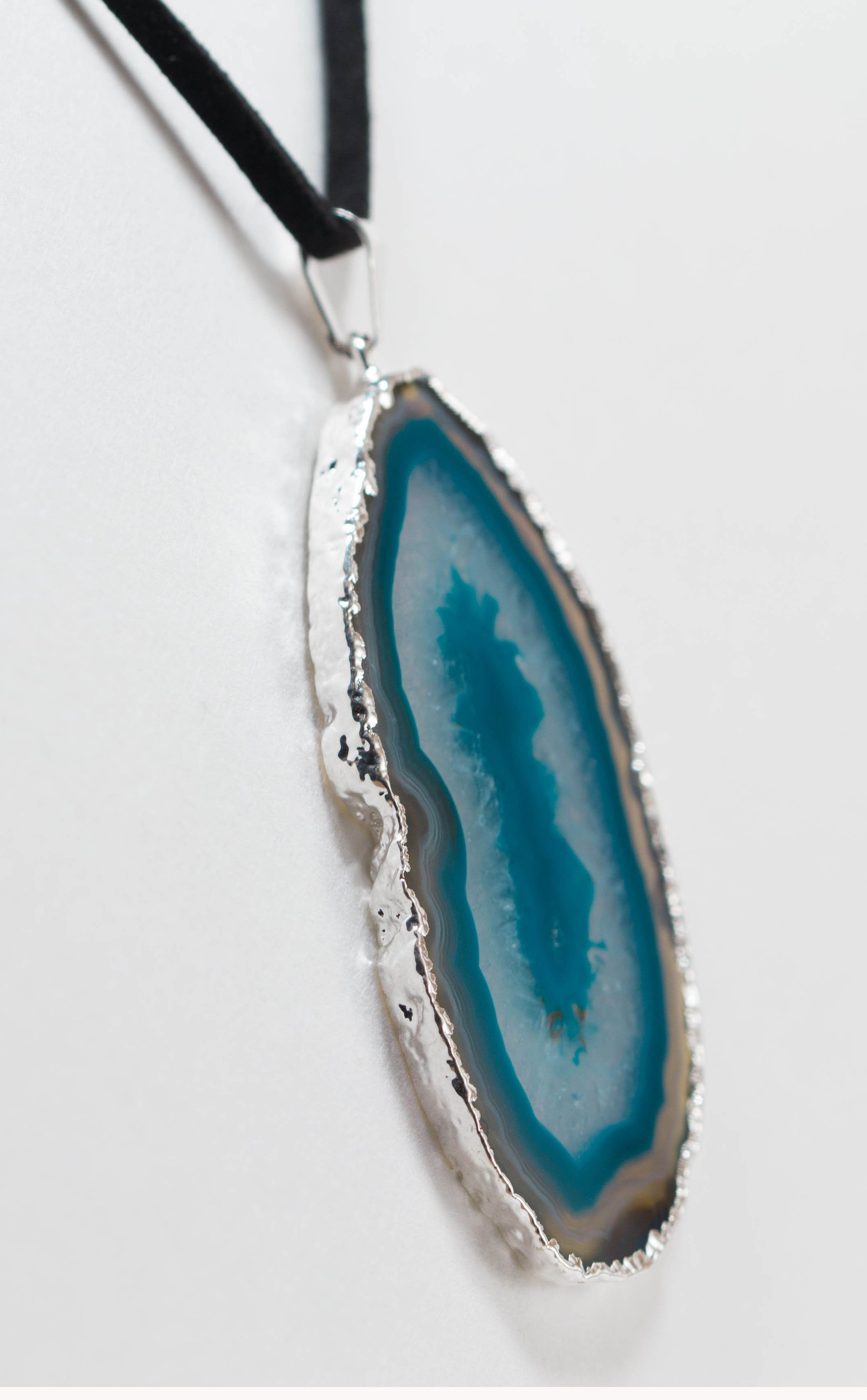 A stylish silver electroplated agate slice pendant hanging from a leather cord, showcasing vibrant colors and unique patterns.