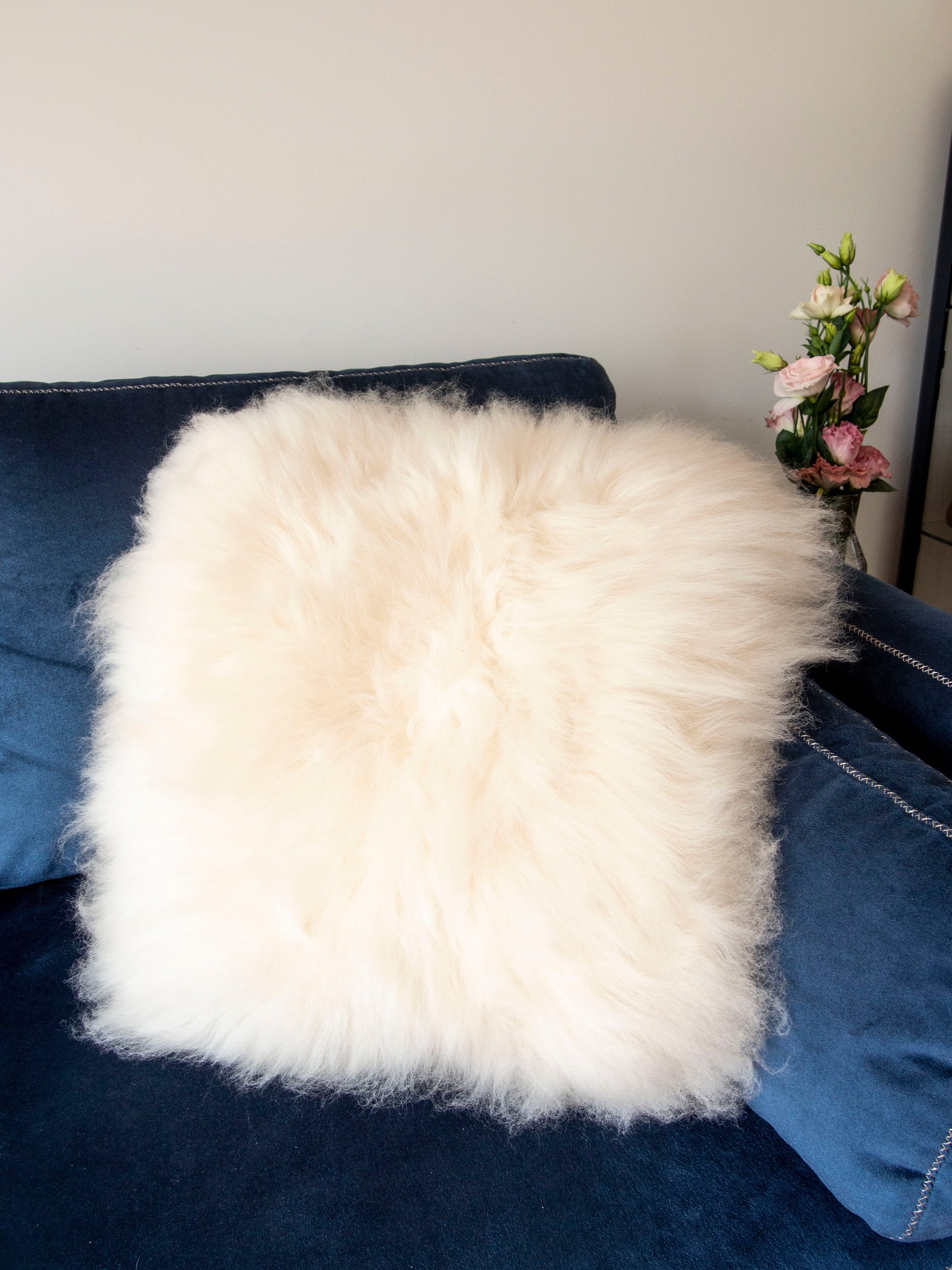 A luxurious square furry pillow made from 100% natural sheepskin, showcasing its soft and fluffy texture in a cozy setting.