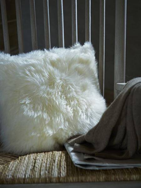 A luxurious square furry pillow made from 100% natural sheepskin, showcasing its soft and fluffy texture in a cozy setting.