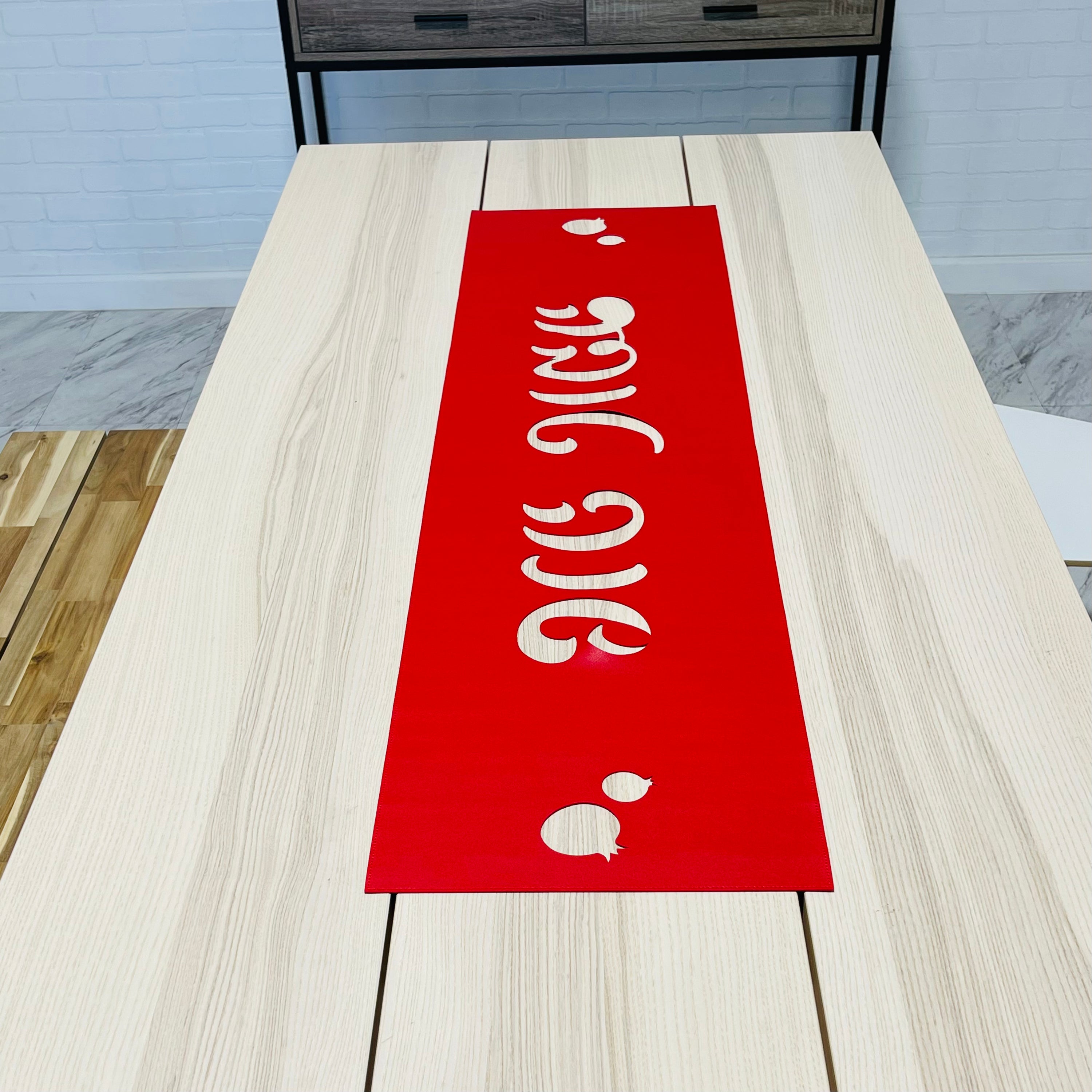 A vibrant laser cut vinyl table runner featuring 'Shana Tova' in Hebrew script, adorned with decorative pomegranates, perfect for Rosh Hashanah.