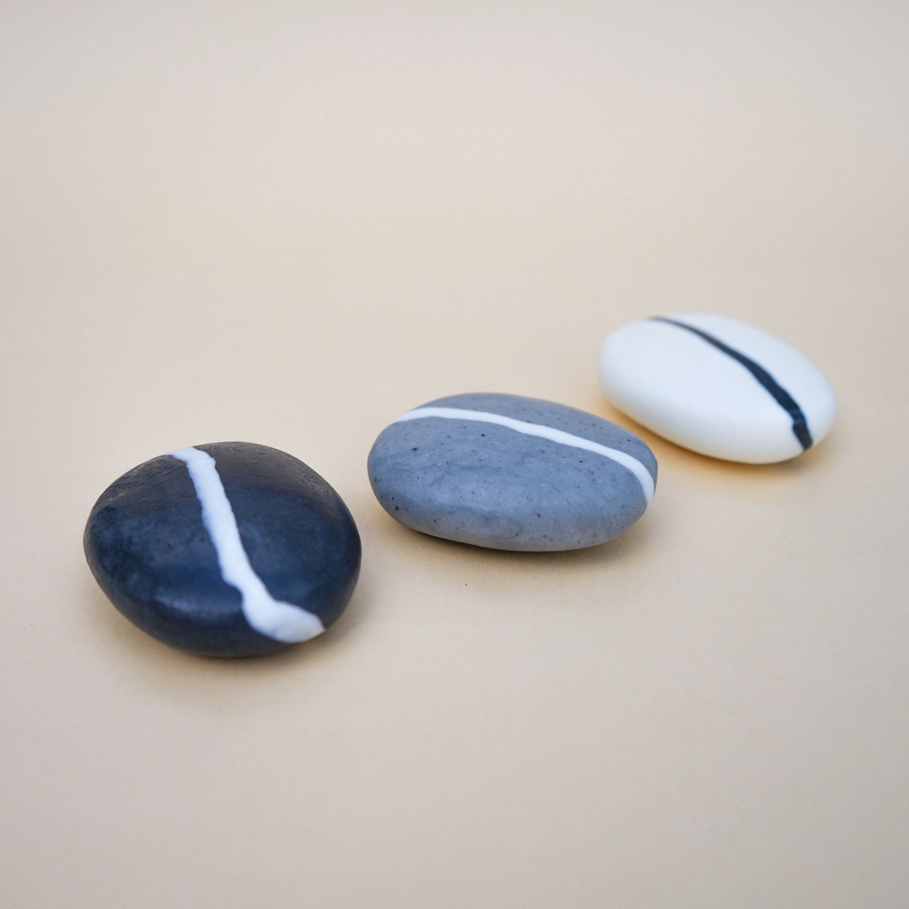 A collection of handmade Stripe Pebble Soaps in various colors and stripe designs, showcasing their unique stone shape and natural beauty.