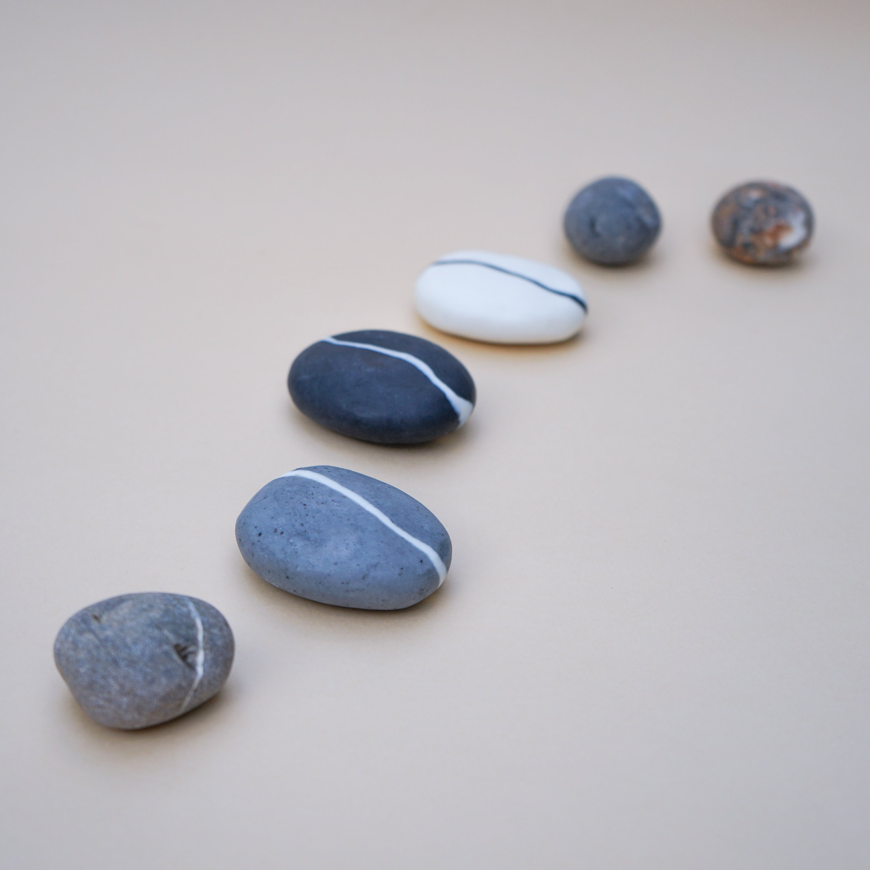 A collection of handmade Stripe Pebble Soaps in various colors and stripe designs, showcasing their unique stone shape and natural beauty.