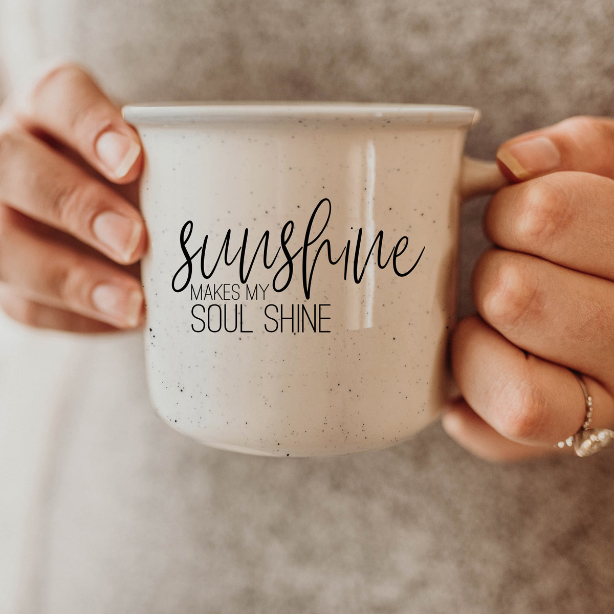 A stylish Sunshine 14.5oz ceramic mug with a white sesame glaze, featuring speckles and black lettering, perfect for outdoor use.