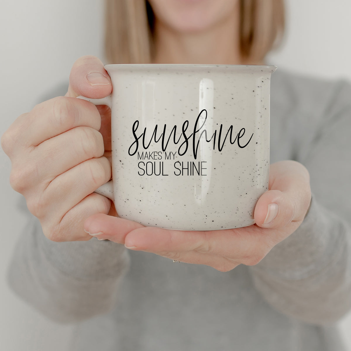 A stylish Sunshine 14.5oz ceramic mug with a white sesame glaze, featuring speckles and black lettering, perfect for outdoor use.