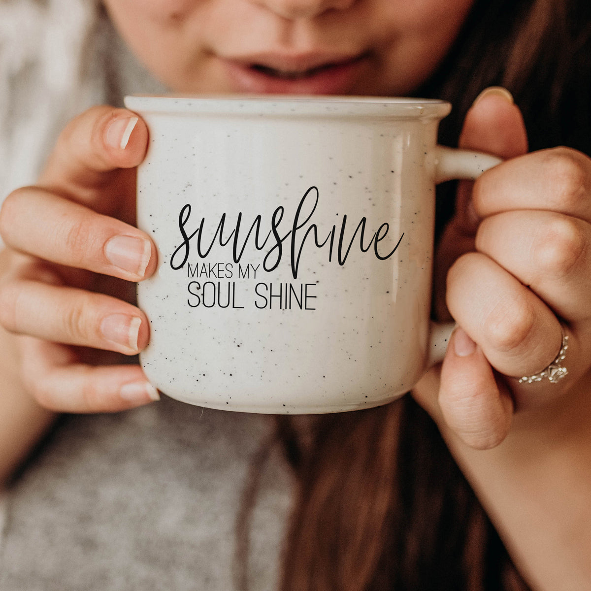 A stylish Sunshine 14.5oz ceramic mug with a white sesame glaze, featuring speckles and black lettering, perfect for outdoor use.