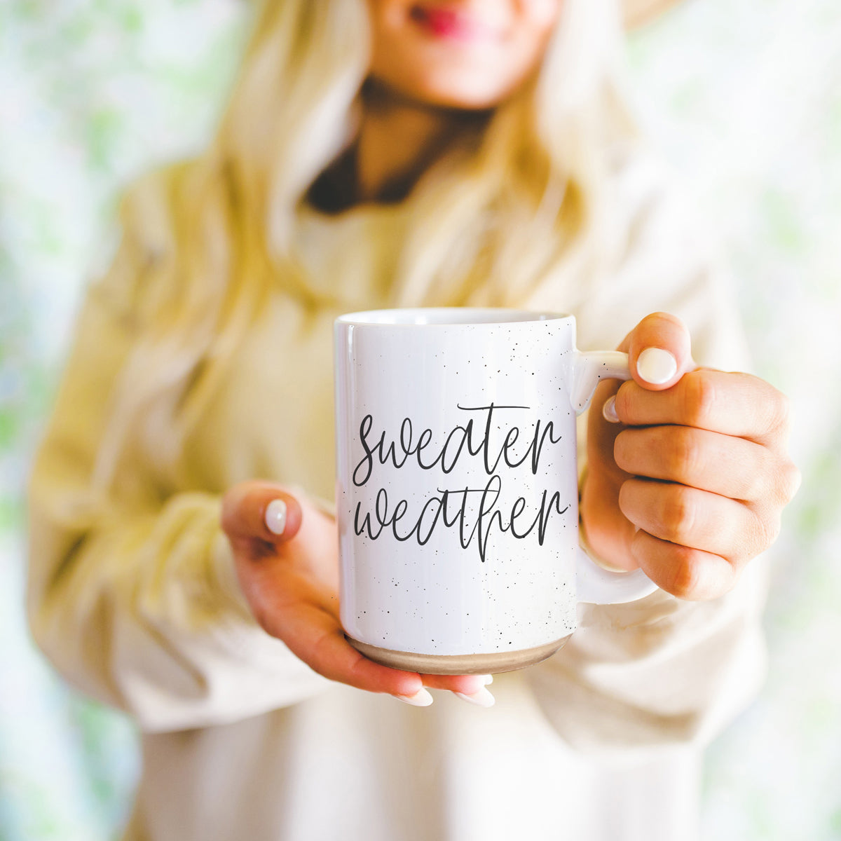 A cozy off-white ceramic mug with dark speckles, featuring a stylish black graphic that reads 'Sweater Weather', perfect for warm beverages.