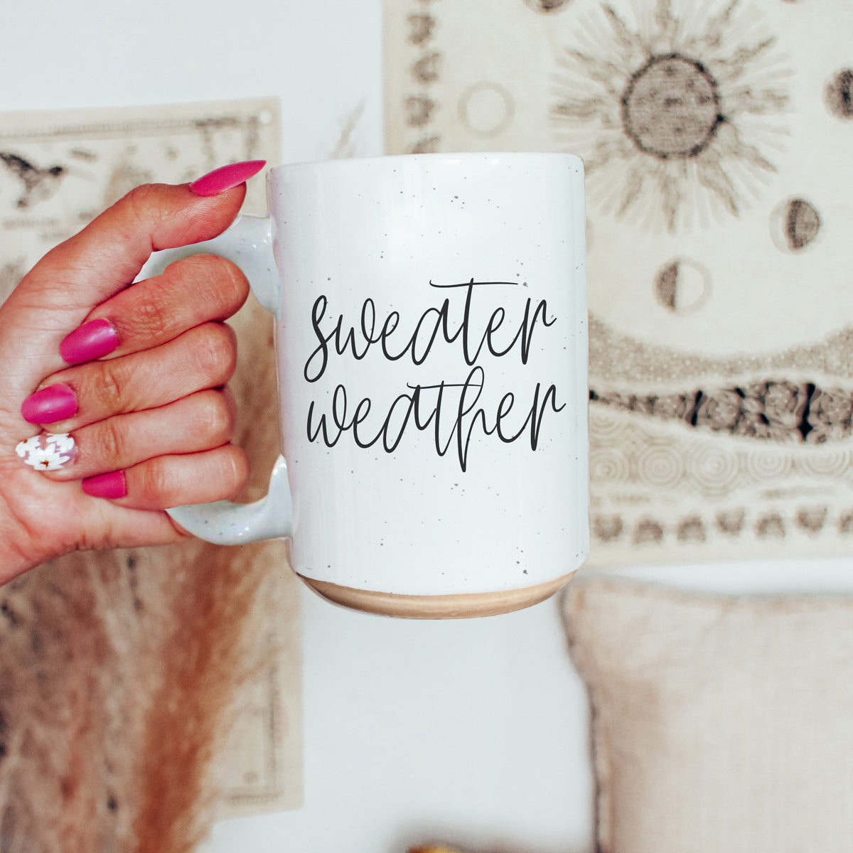 A cozy off-white ceramic mug with dark speckles, featuring a stylish black graphic that reads 'Sweater Weather', perfect for warm beverages.