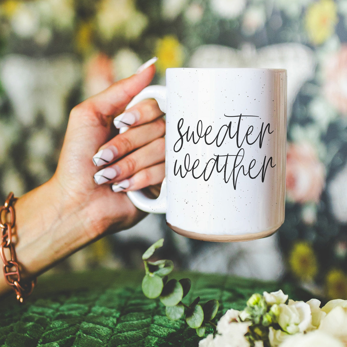 A cozy off-white ceramic mug with dark speckles, featuring a stylish black graphic that reads 'Sweater Weather', perfect for warm beverages.