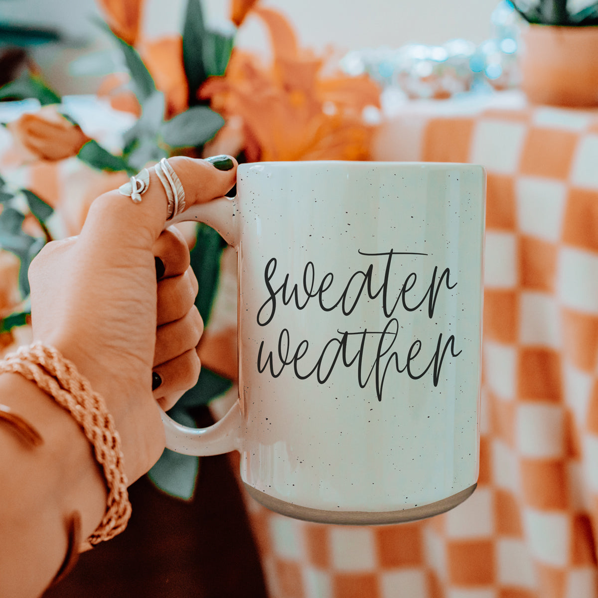 A cozy off-white ceramic mug with dark speckles, featuring a stylish black graphic that reads 'Sweater Weather', perfect for warm beverages.