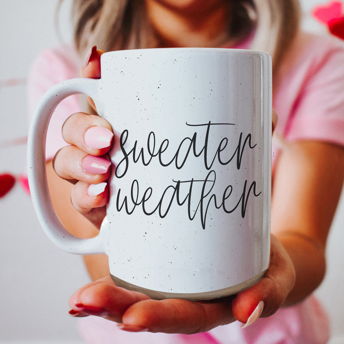 A cozy off-white ceramic mug with dark speckles, featuring a stylish black graphic that reads 'Sweater Weather', perfect for warm beverages.