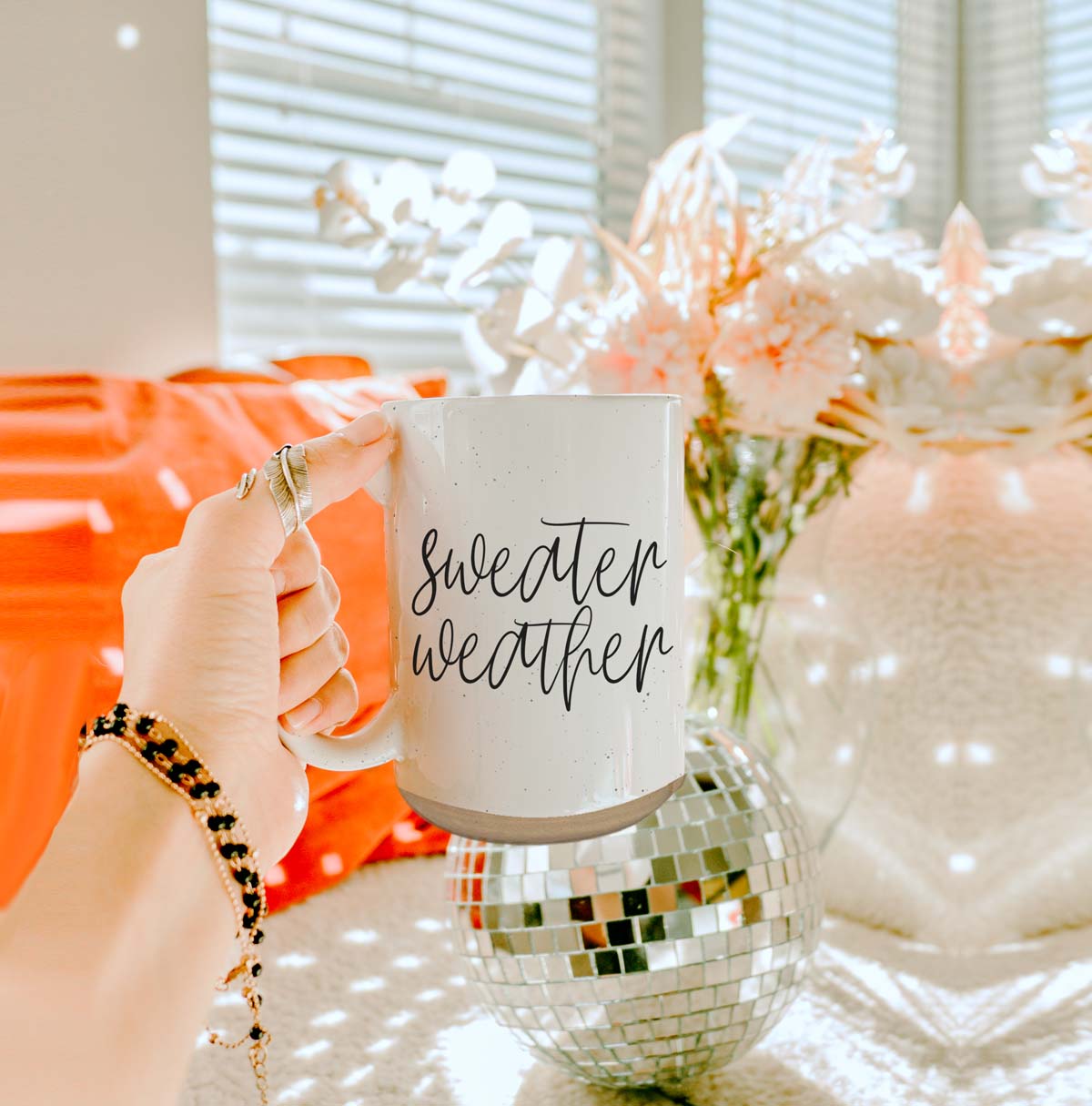 A cozy off-white ceramic mug with dark speckles, featuring a stylish black graphic that reads 'Sweater Weather', perfect for warm beverages.