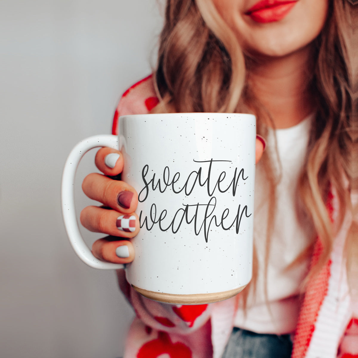 A cozy off-white ceramic mug with dark speckles, featuring a stylish black graphic that reads 'Sweater Weather', perfect for warm beverages.