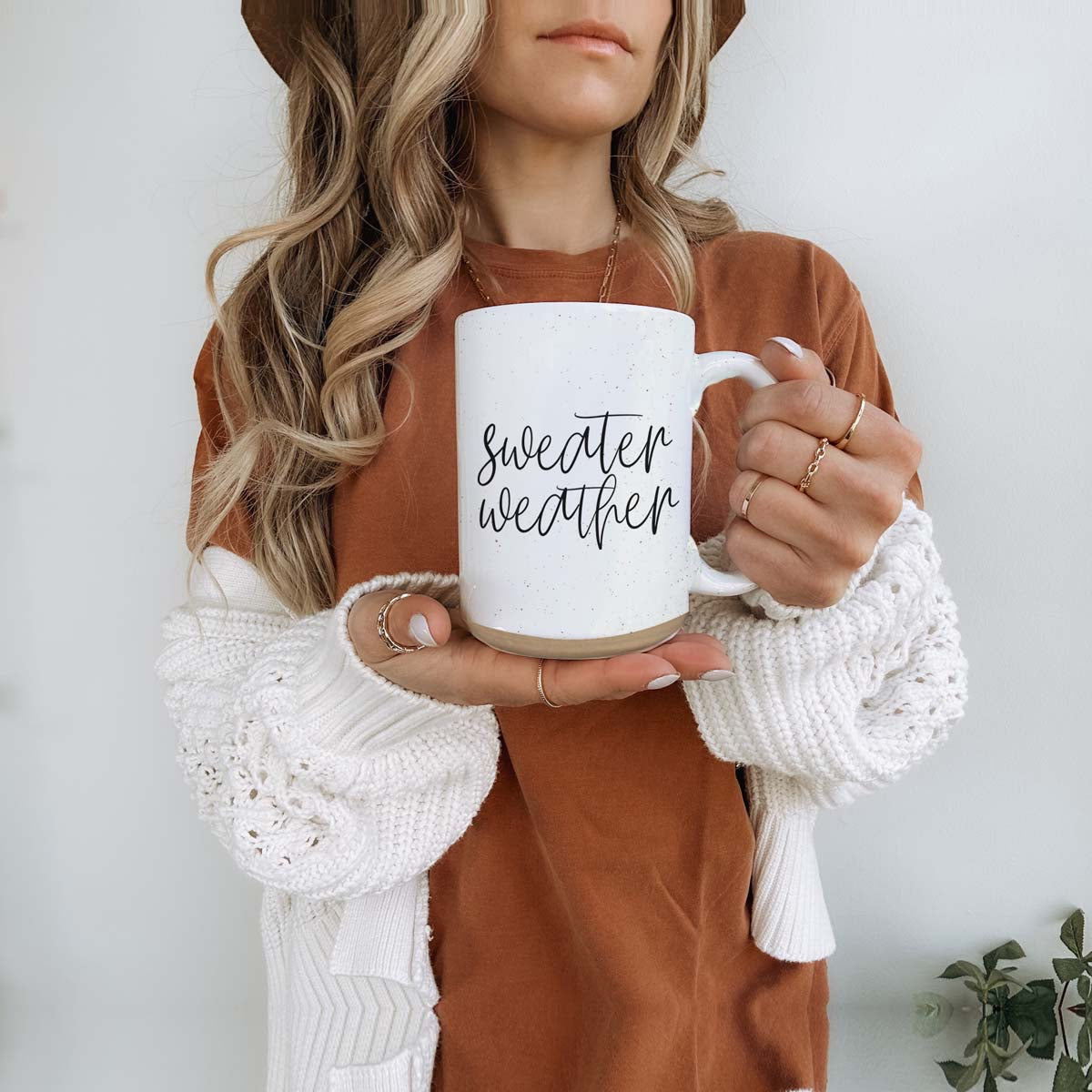 A cozy off-white ceramic mug with dark speckles, featuring a stylish black graphic that reads 'Sweater Weather', perfect for warm beverages.