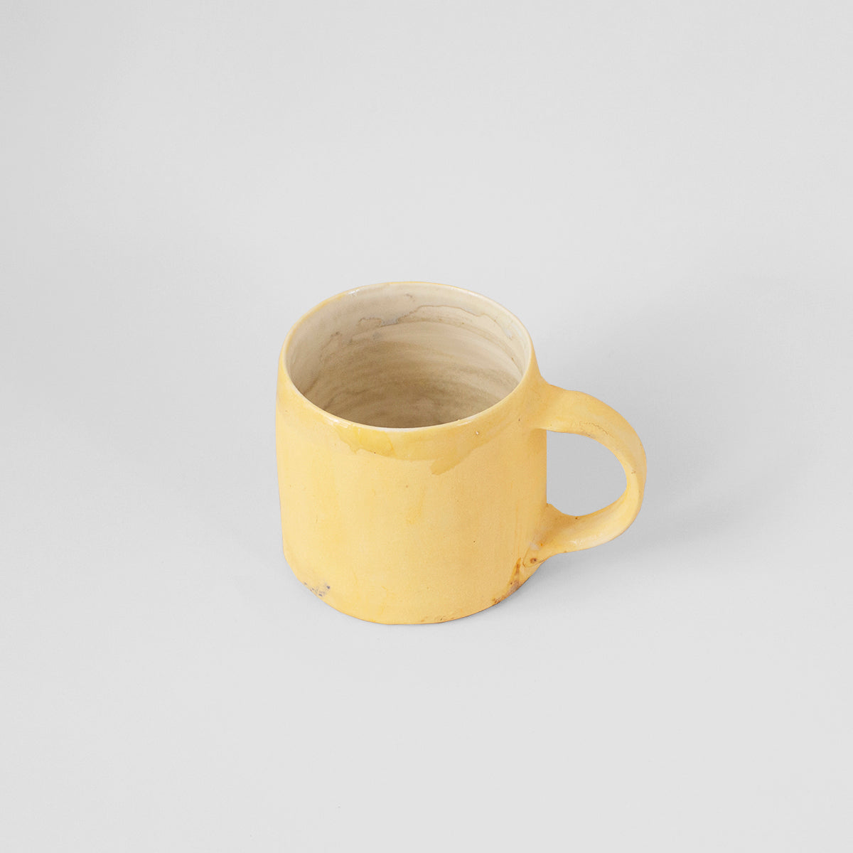 A vibrant yellow handmade ceramic mug by Gunvor Tangrand, showcasing unique glaze and design inspired by Lofoten's nature.