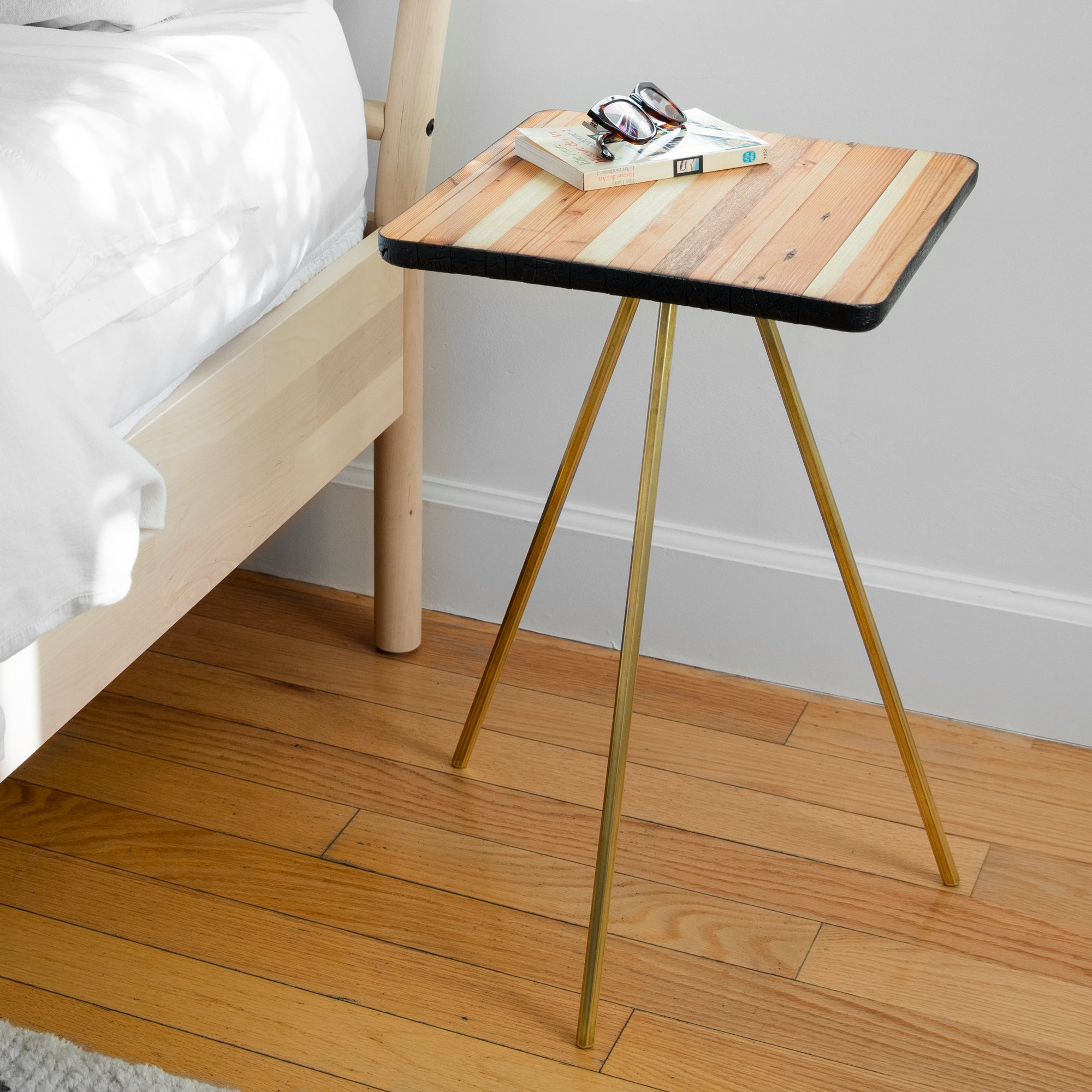 Tantric side table featuring sleek brass legs and a reclaimed wood top with a torched black and natural finish.