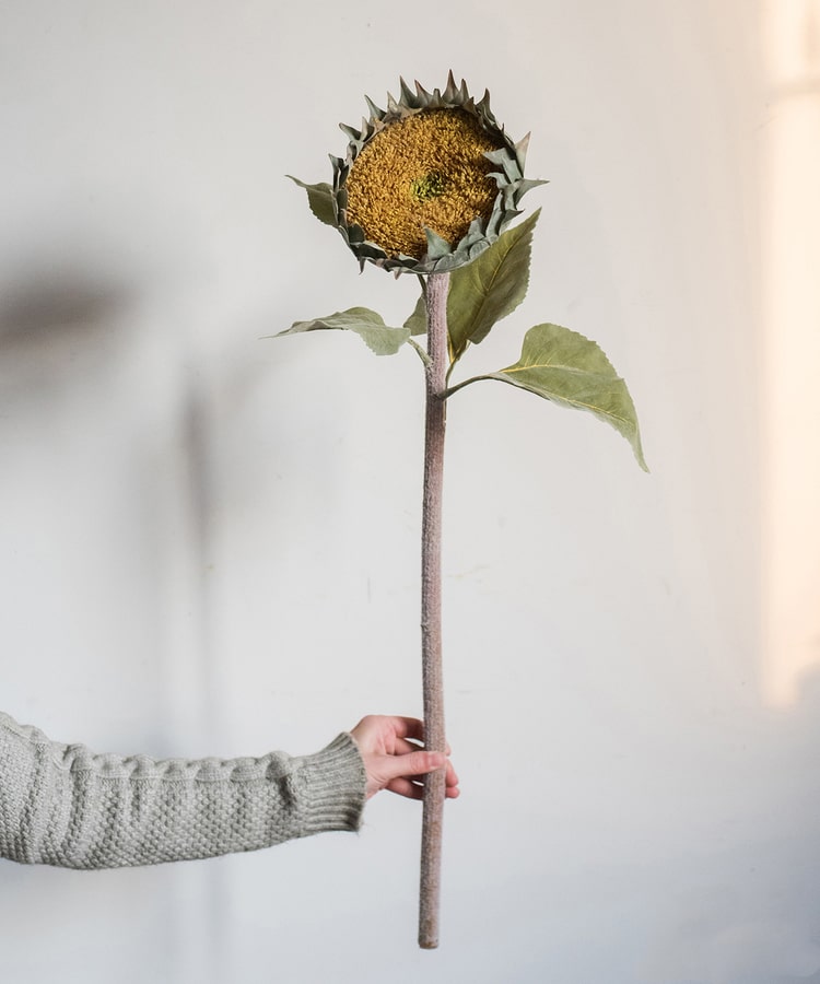 A beautiful handmade artificial sunflower stem with vibrant yellow petals, green leaves, and a brown stem, perfect for home decor.