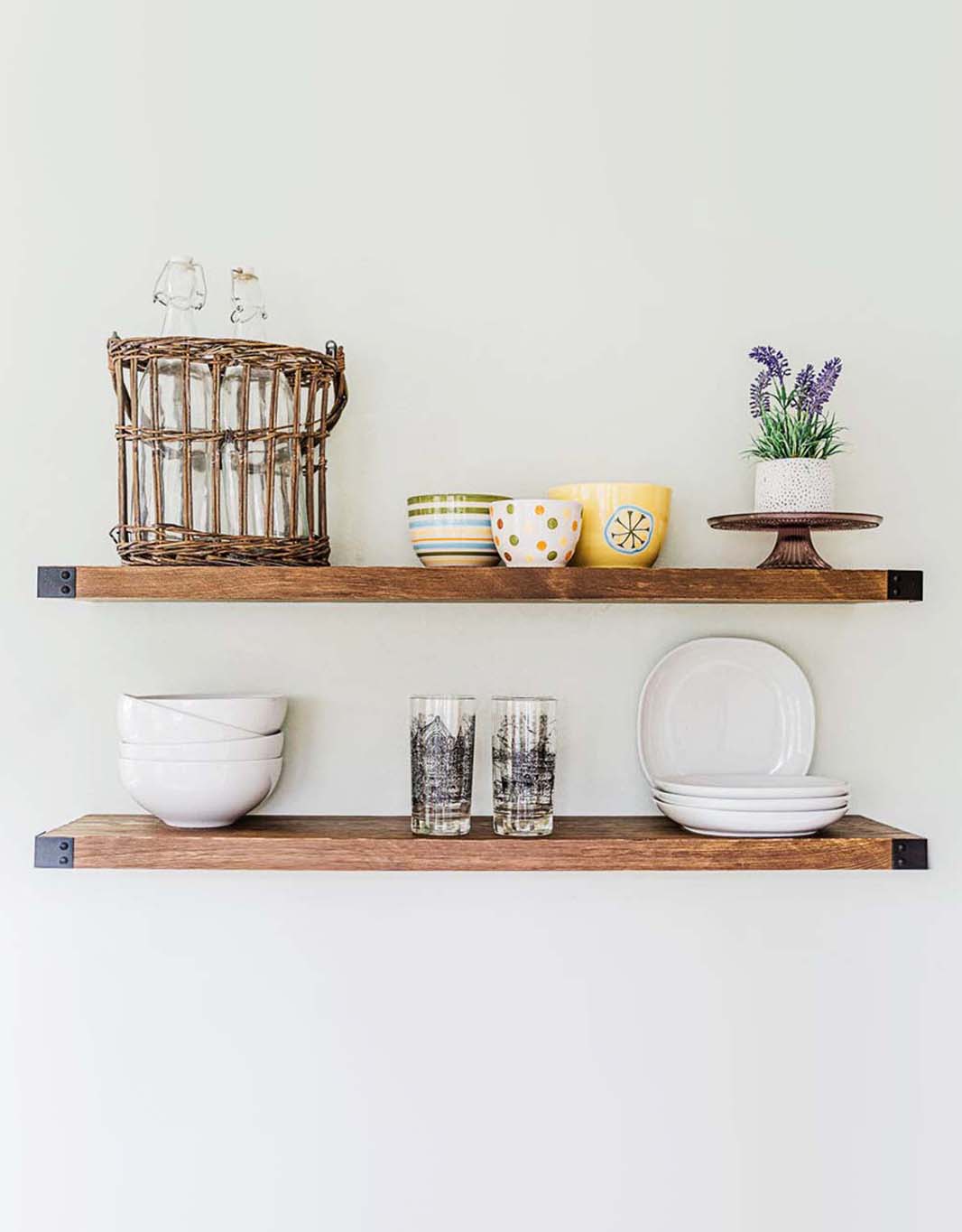 The Sylvia floating shelves showcasing a modern rustic design with light walnut stain and industrial iron brackets, mounted on a wall.