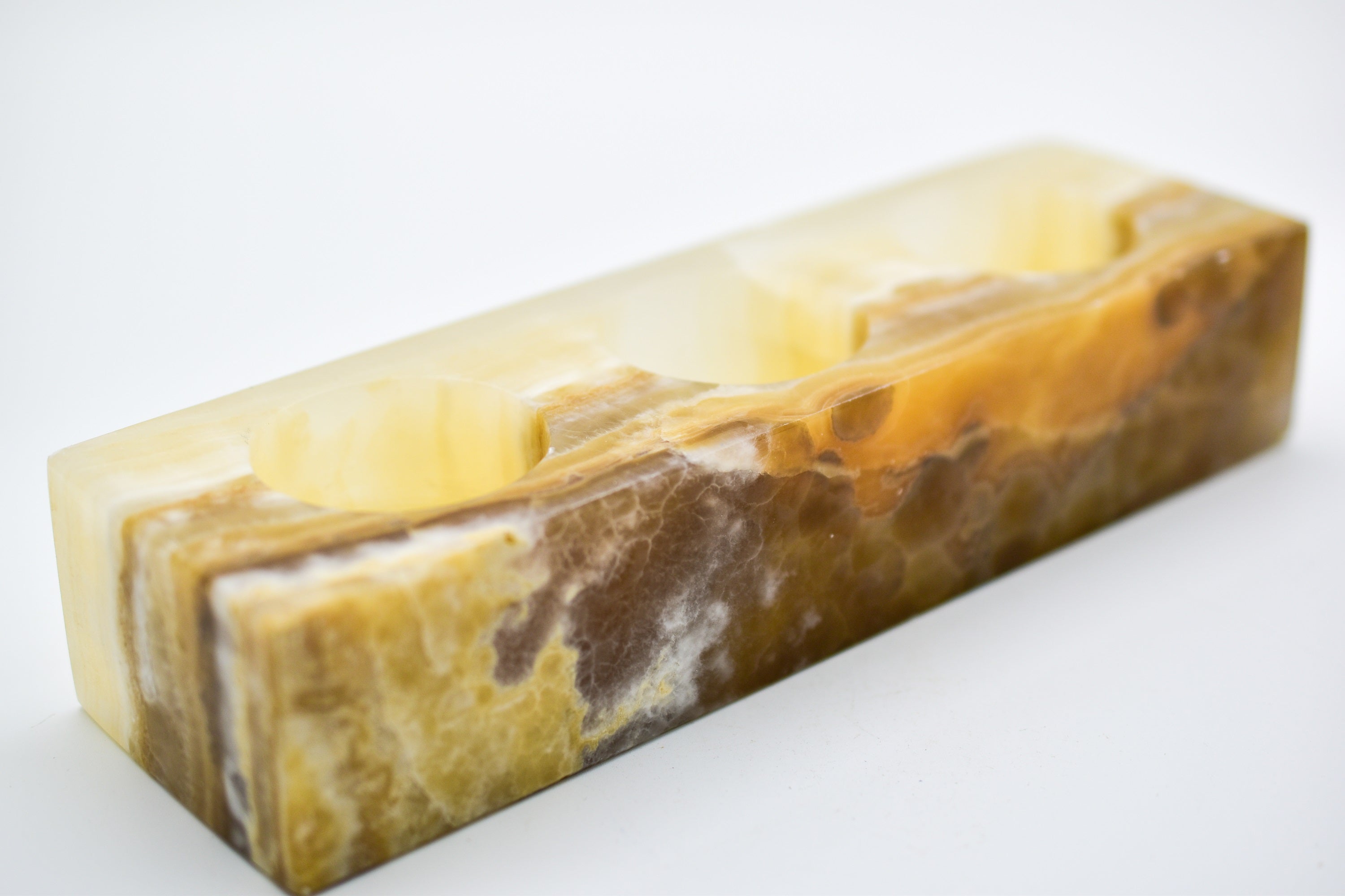 A rectangular triple votive candle holder made from natural onyx, showcasing unique colors and patterns, designed to hold three 1.5" diameter candles.