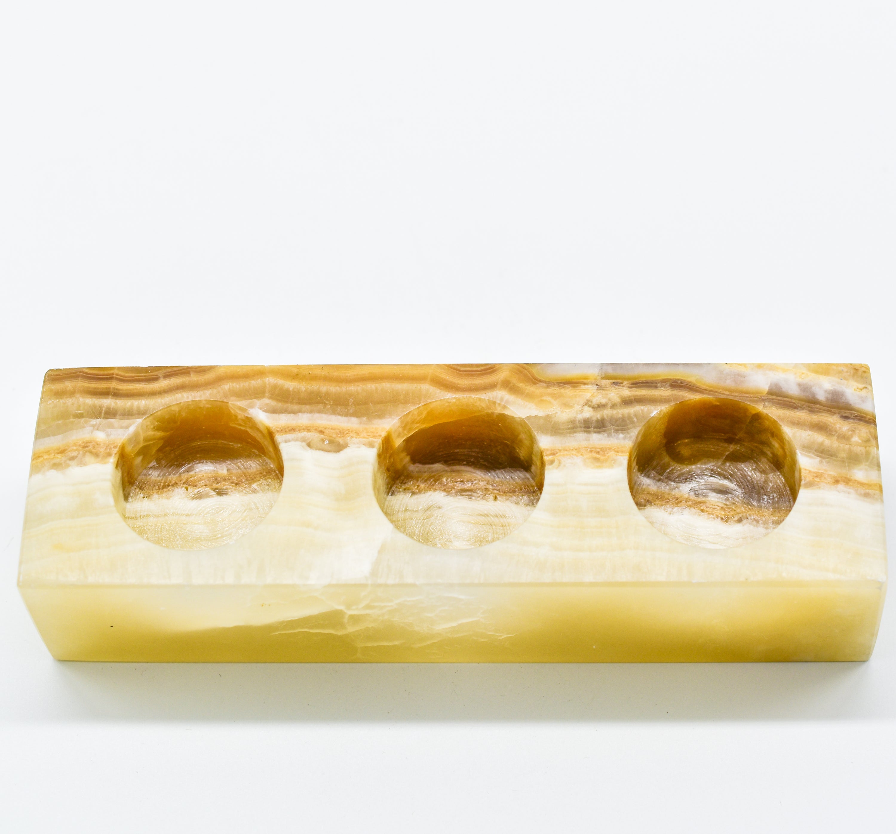 A rectangular triple votive candle holder made from natural onyx, showcasing unique colors and patterns, designed to hold three 1.5" diameter candles.