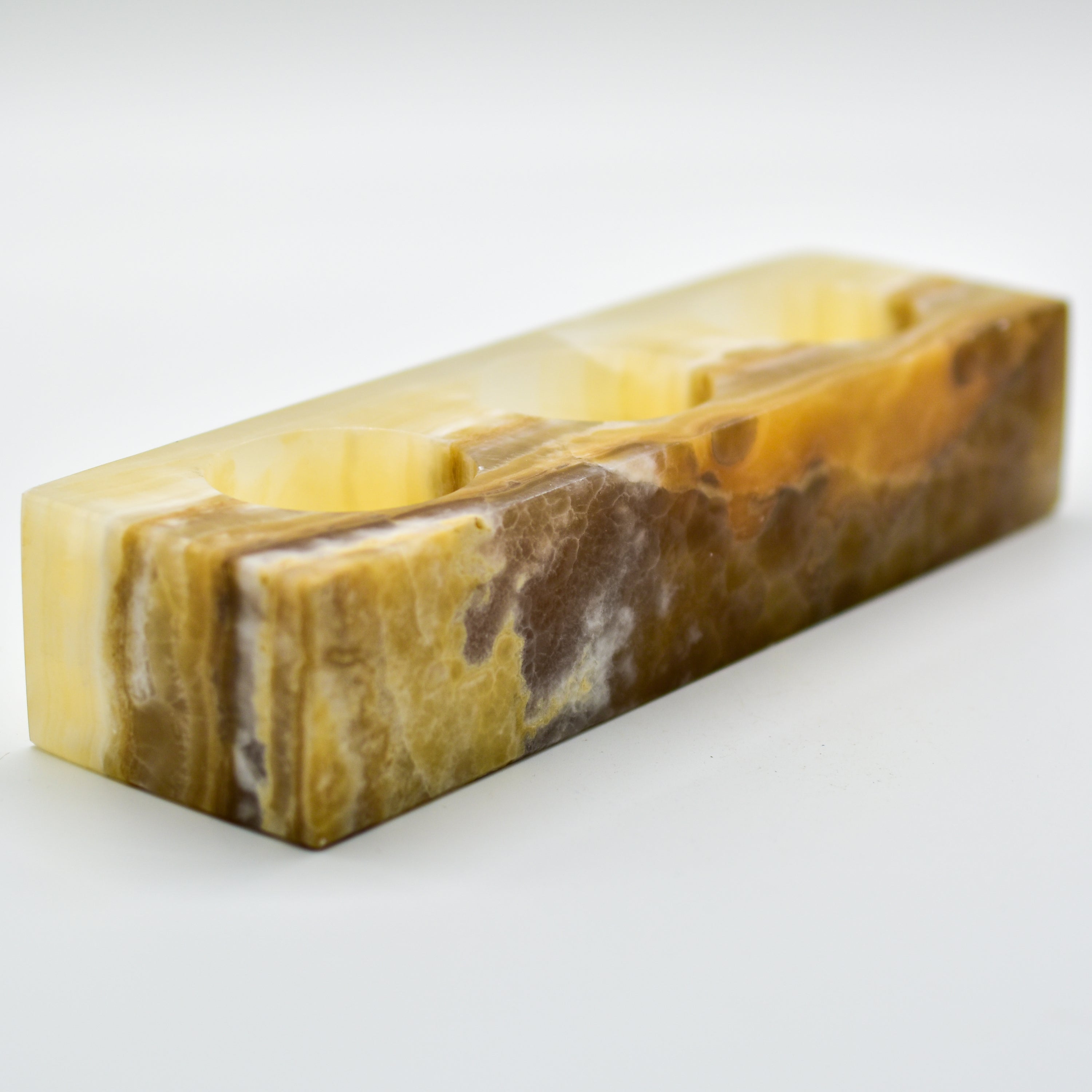 A rectangular triple votive candle holder made from natural onyx, showcasing unique colors and patterns, designed to hold three 1.5" diameter candles.