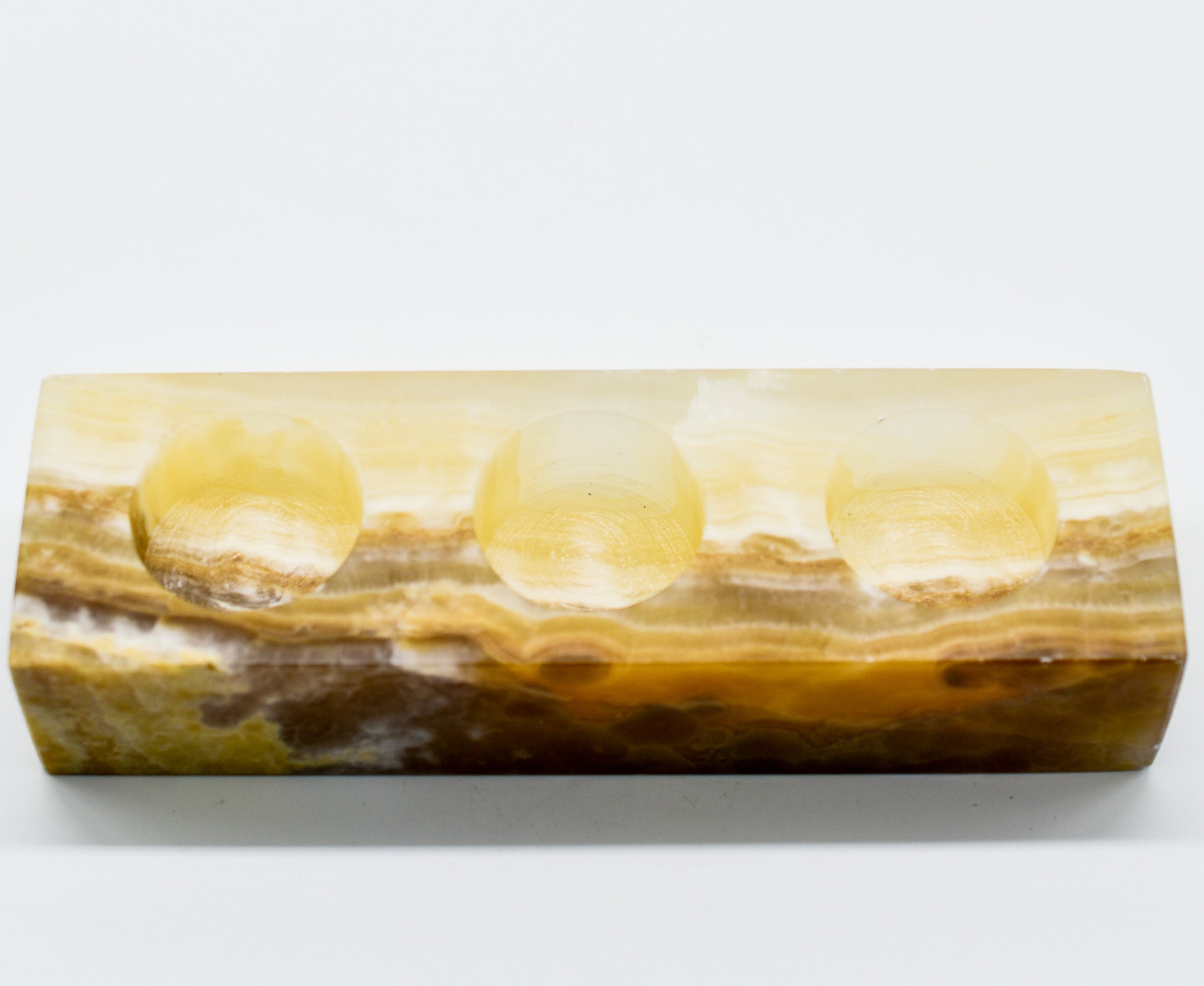 A rectangular triple votive candle holder made from natural onyx, showcasing unique colors and patterns, designed to hold three 1.5" diameter candles.