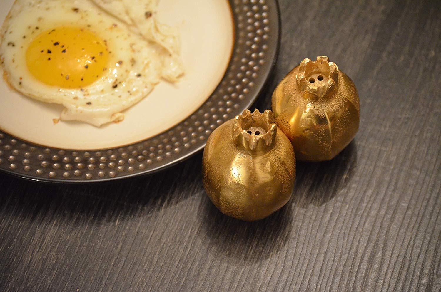 Handcrafted golden napkin holder with olive bud design and unique pomegranate salt and pepper shakers, elegantly displayed on a dining table.