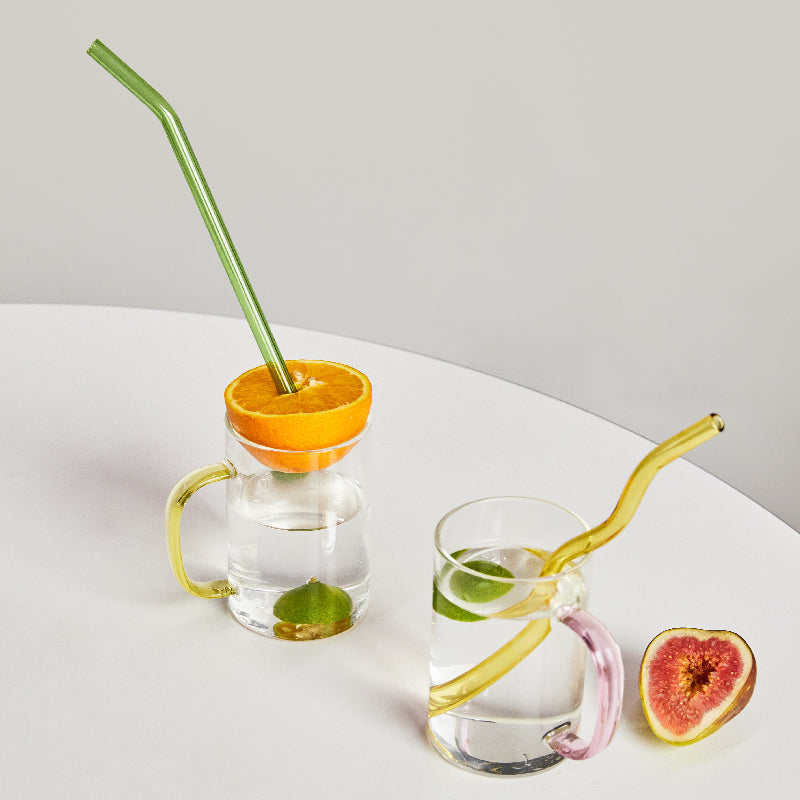 A set of elegant wavy glass straws in various colors, showcasing their unique curved design and included cleaning brush.