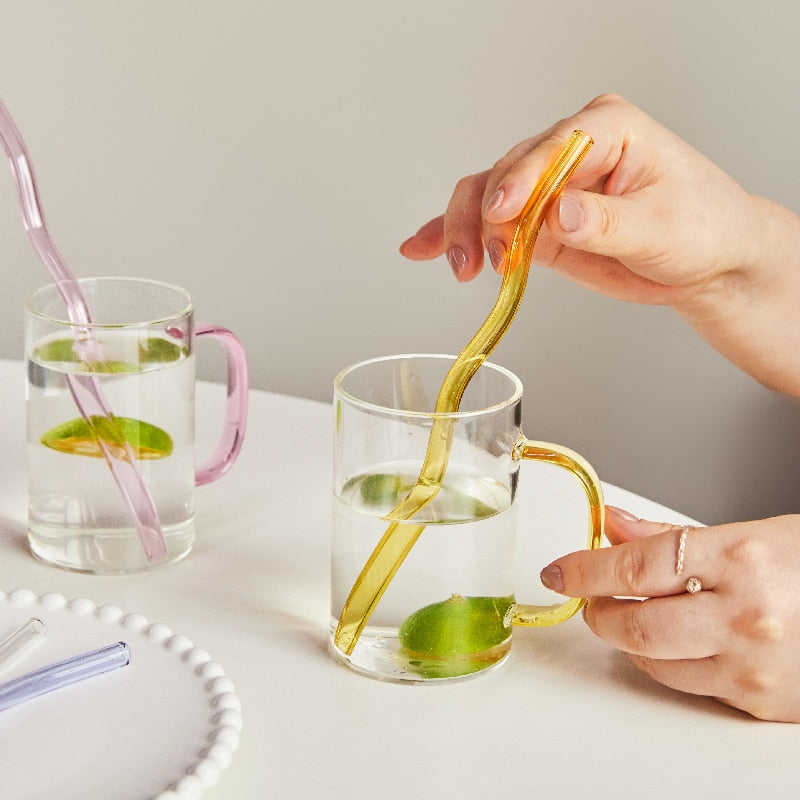 A set of elegant wavy glass straws in various colors, showcasing their unique curved design and included cleaning brush.