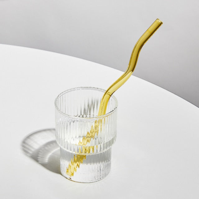 A set of elegant wavy glass straws in various colors, showcasing their unique curved design and included cleaning brush.